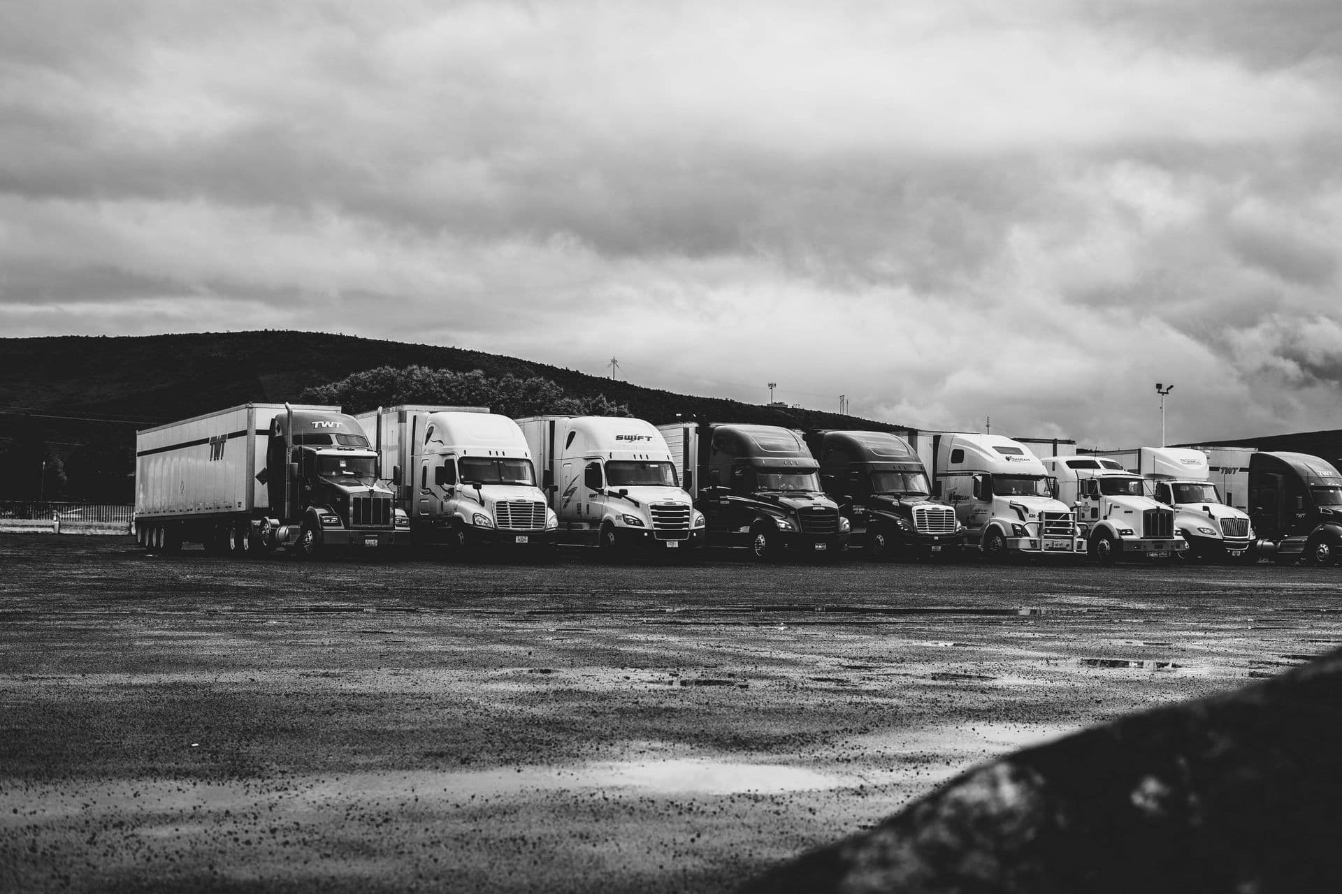 Row of prime movers parked on a wet depot lot under a stormy sky