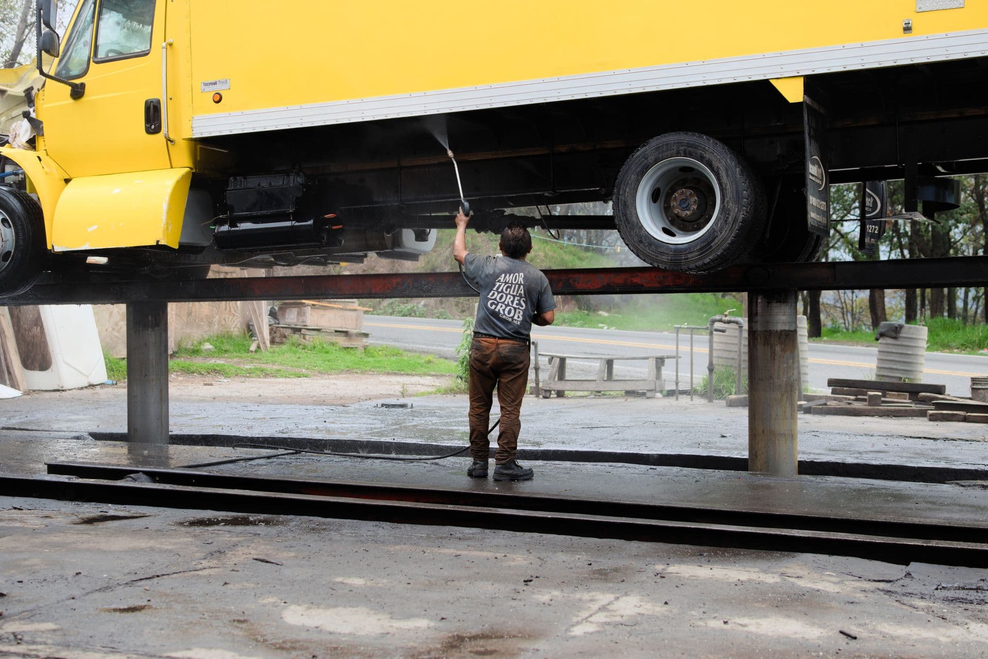 Worker power-washing the underside of a raised truck